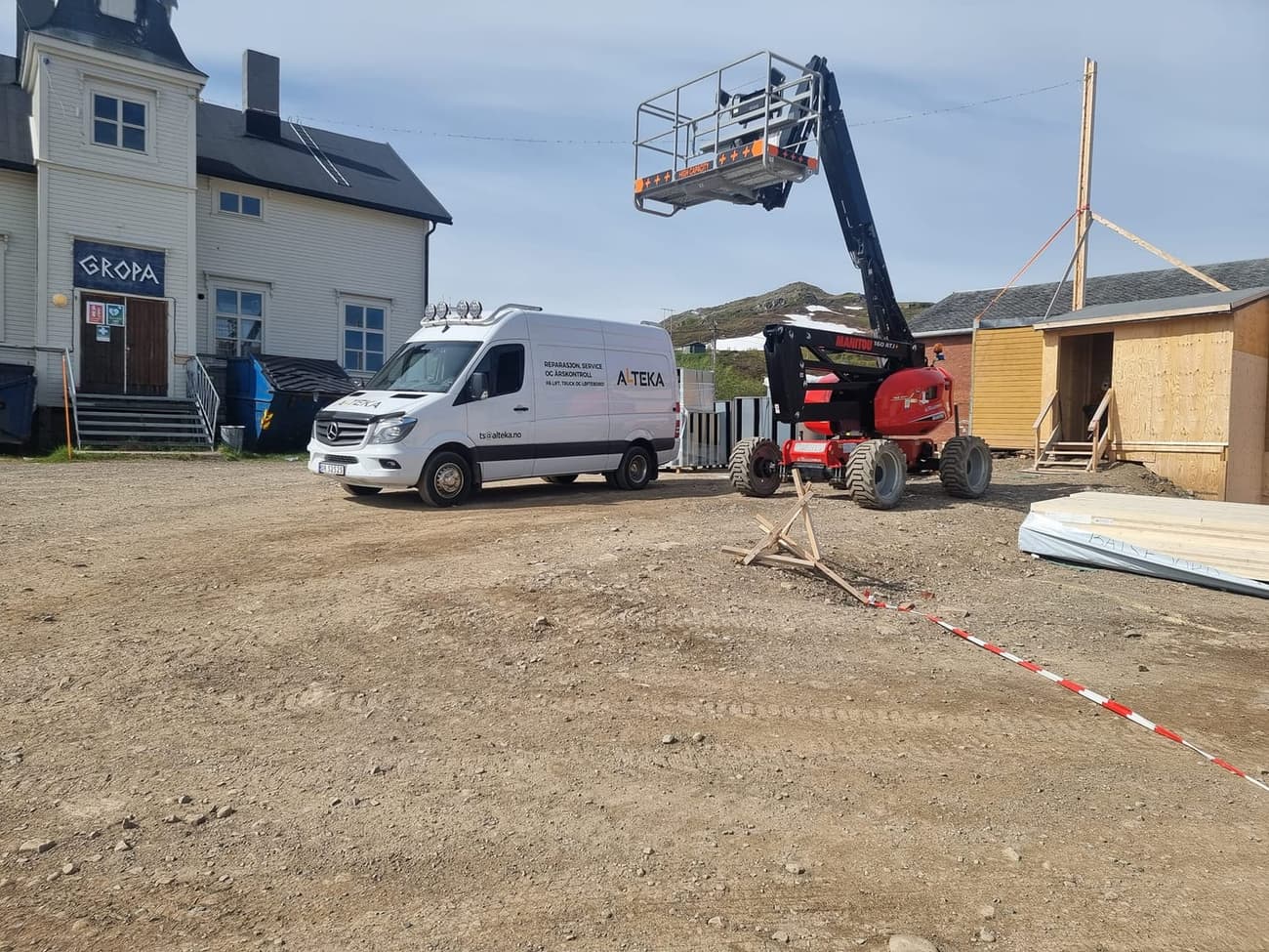 Servicebilen ved siden av en rød Manitou bomlift med kurven hevet på en byggeplass