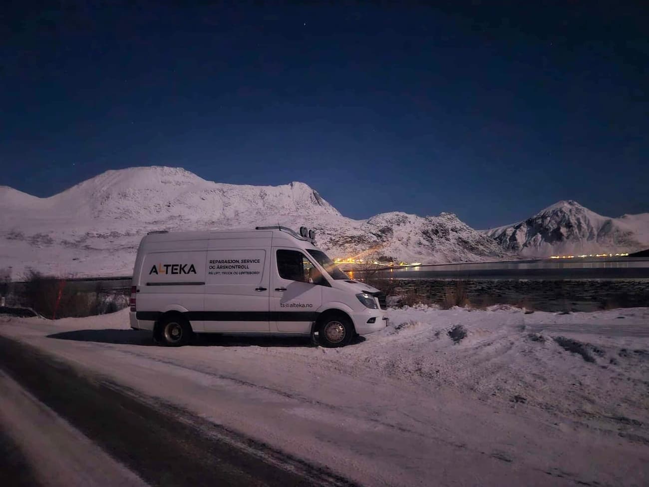 Servicebilen på vei ut på oppdrag langs fjorden, med snødekte fjell i bakgrunnen